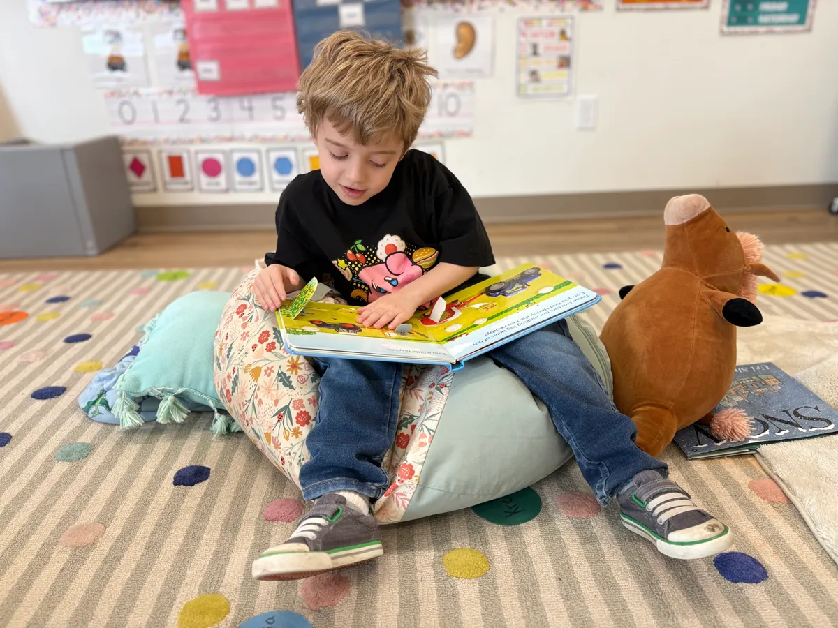 A preschooler reading independently on a beanbag at Spark Academy