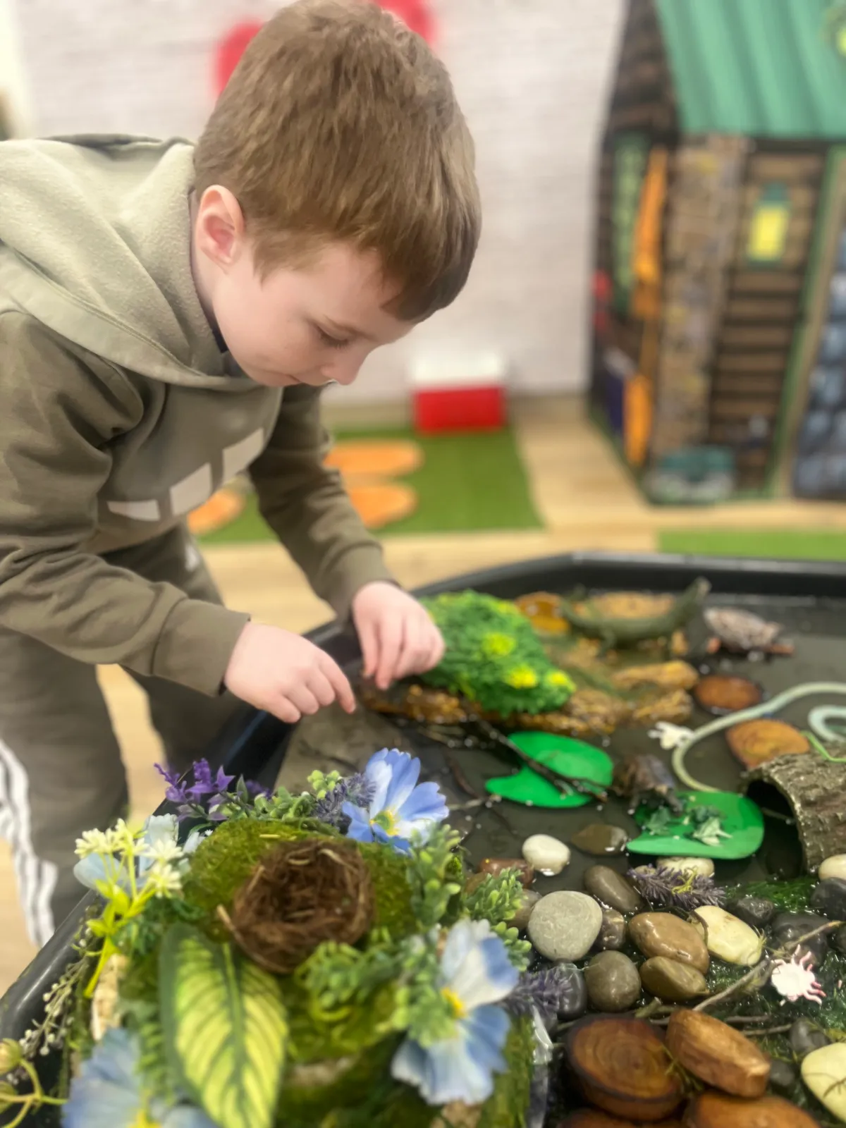 Child exploring a nature pond sensory table in the Developmental Playroom at Spark Academy