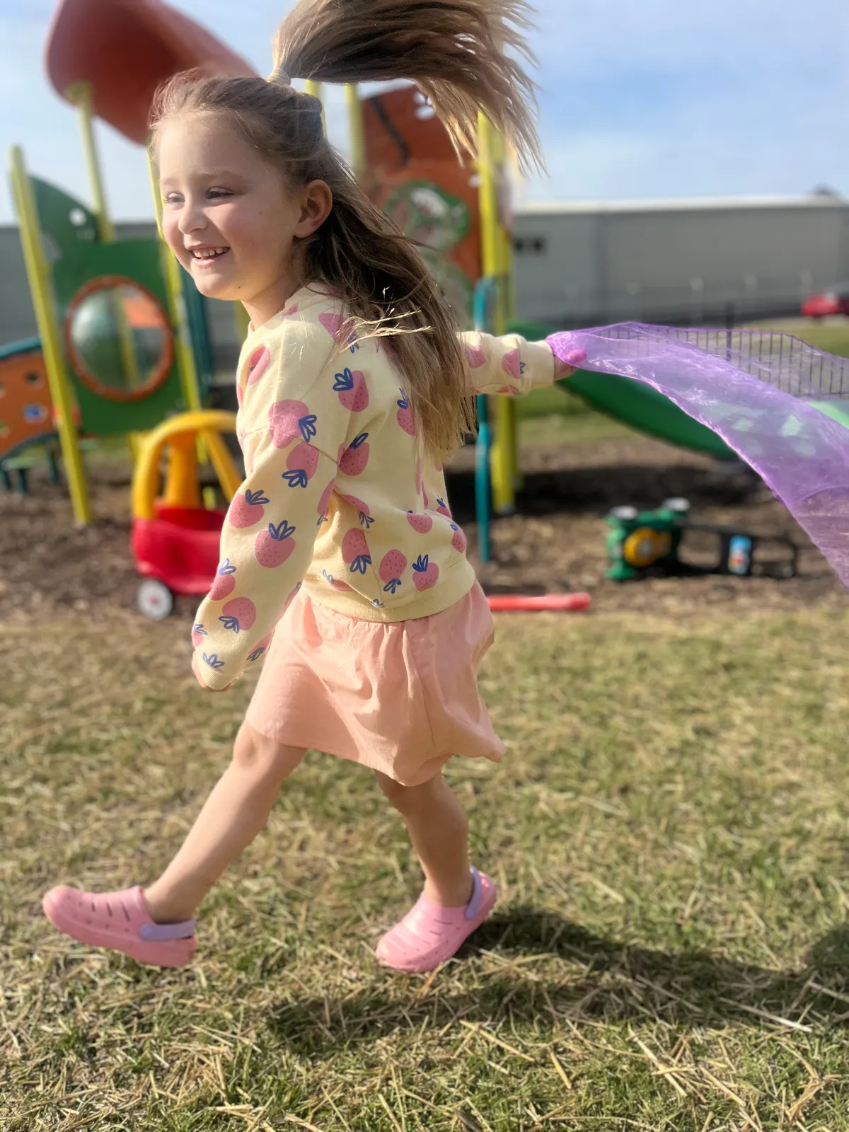 Child running with a scarf flowing behind her on the playground at Spark Academy Camp Play