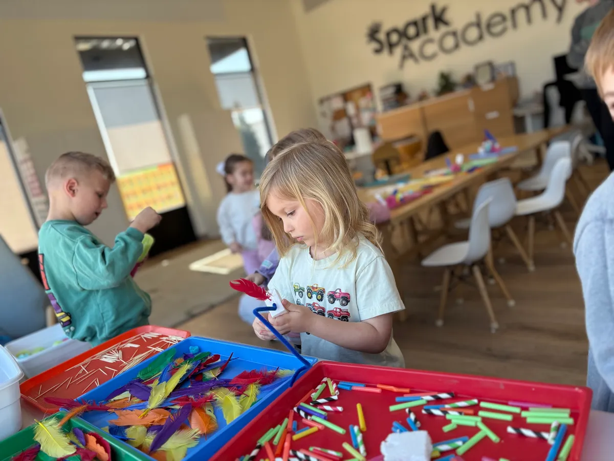 Three-year-old child picking art supplies during hands-on learning activity at Spark Academy