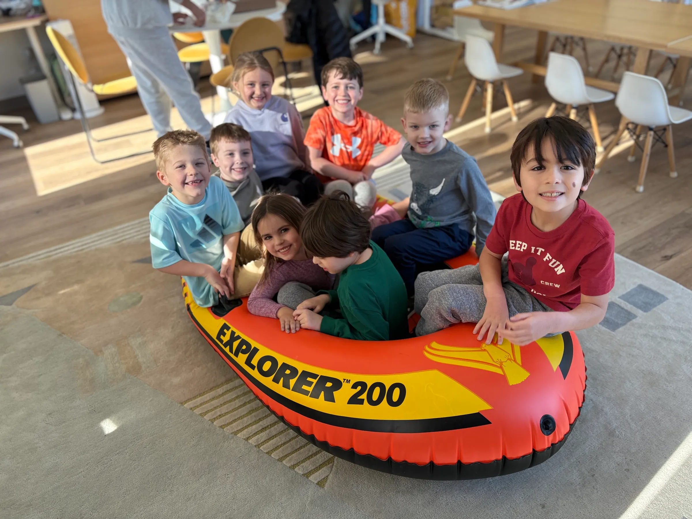 A group of Spark Academy students packed into an inflatable boat in the Developmental Playroom — learning through play